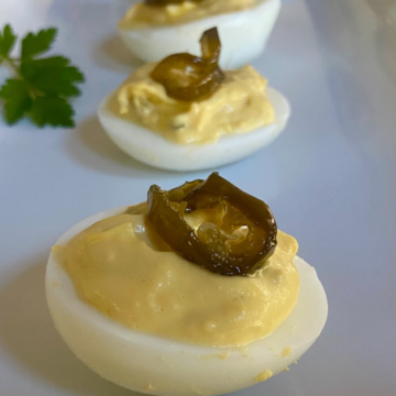 Garnish each Hot and Sweet Jalapeño Deviled Egg with a slice of hot and sweet jalapeño for flavor and presentation.